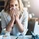 Woman at her desk sneezing as she is attempting to get back to work after a cold.
