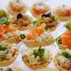Small, elegant appetizers are beautifully arranged on a platter. Various toppings, including salmon and seafood, create an inviting display for guests at a celebration.