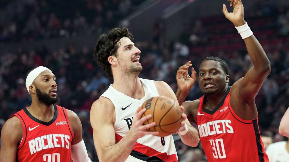 Portland Trail Blazers forward Deni Avdija, center, drives to the basket between Houston Rockets center Clint Capela, right, and guard Josh Okogie during the first half of an NBA basketball game in Portland, Ore., Wednesday, Jan. 7, 2026. (AP Photo/Craig Mitchelldyer)