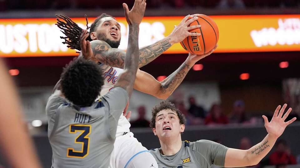 Houston's Emanuel Sharp, center, goes up for a shot as West Virginia's Honor Huff (3) and Treysen Eaglestaff (52) defend during the second half of an NCAA college basketball game Tuesday, Jan. 13, 2026, in Houston. (AP Photo/David J. Phillip)