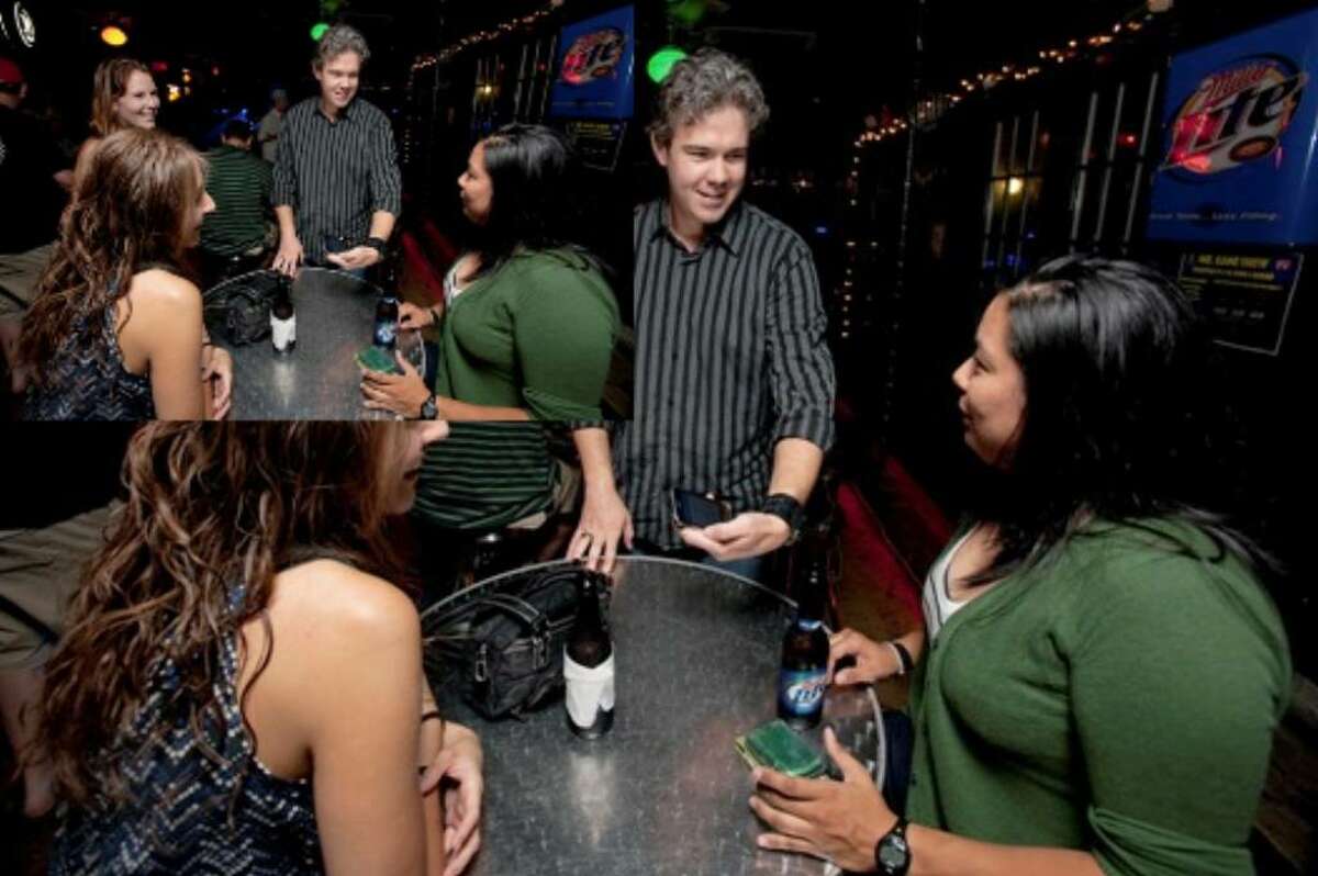 Bret McGowen (center) and Amy Collins (left, rear) try to get patrons of Rebar to take on a task that the app BarCards has suggested on their I Phone.