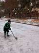 Everett Dean dressed in Dallas Stars gear practices hockey on an iced-over residential street in Austin, Texas.