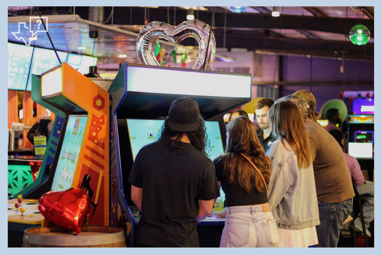 A group of singles crowds around the Killer Queen arcade game at a pre-Valentine's Day mixer hosted by Cidercade in the East End on Feb. 12, 2026, in Houston.