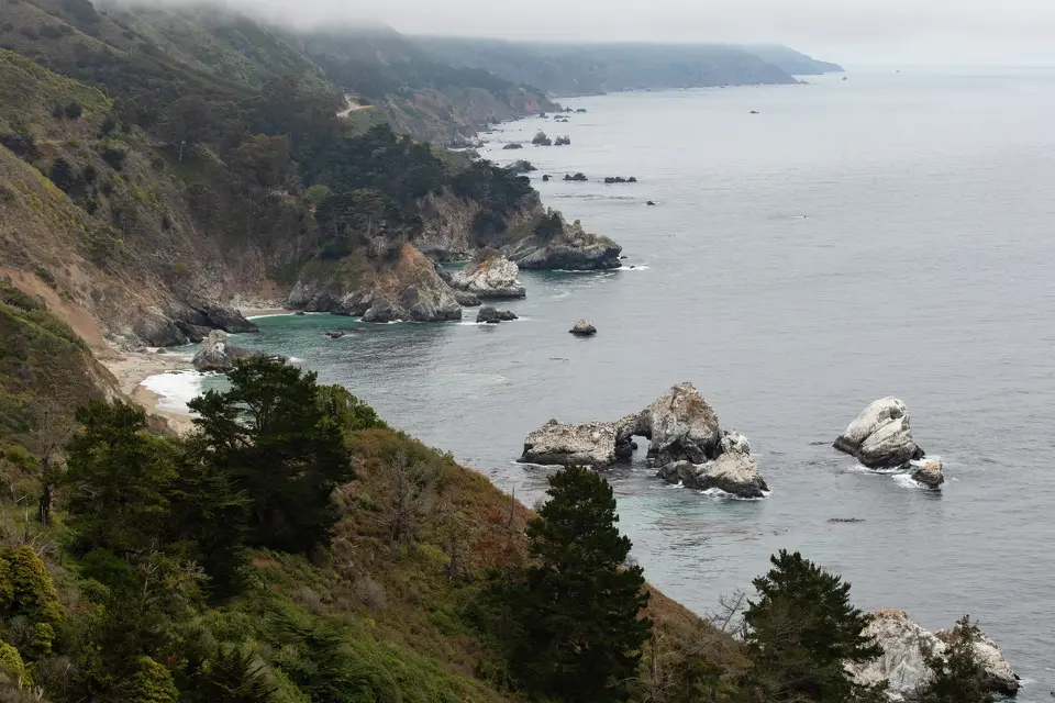 A stretch of Big Sur’s coastline extends south in June 2025, with sea arches and cypress pines sitting below coastal clouds.