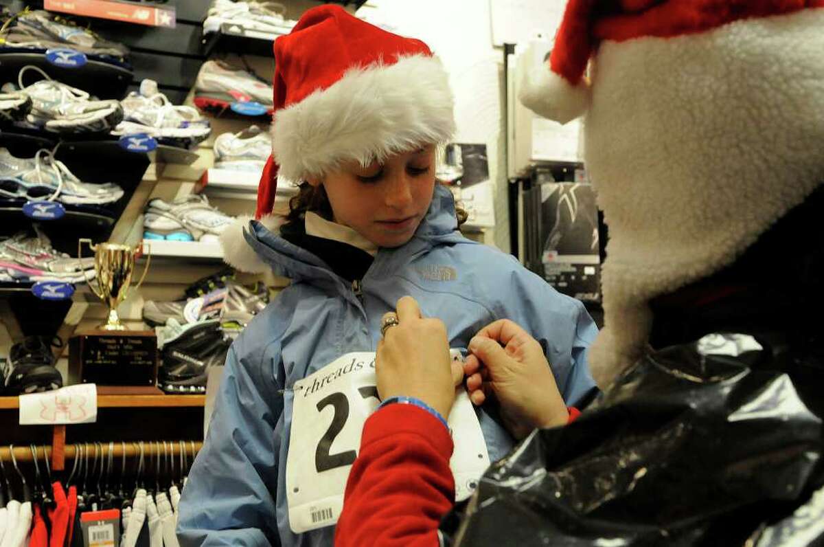 Susan Fahey helps her daughter Grace, 10, attach her race bib in Threads & Treads store. About a hundred people brave the rain and wind for the Jingle Bell Jog in Greenwich CT on Sunday December 12, 2010. Presented by Threads & Treads, and sponsored by Volvo of Stamford, the race is part of the Greenwich Cup 2010 race series. The race started and ended in front of Peabody's Garage on Church Street.