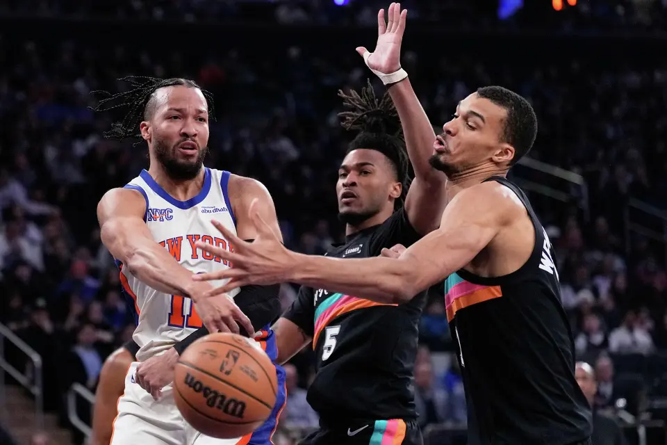 New York Knicks' Jalen Brunson, left, passes around San Antonio Spurs' Victor Wembanyama, right, and Stephon Castle during the first half of an NBA basketball game Sunday, March 1, 2026, in New York. (AP Photo/Seth Wenig)
