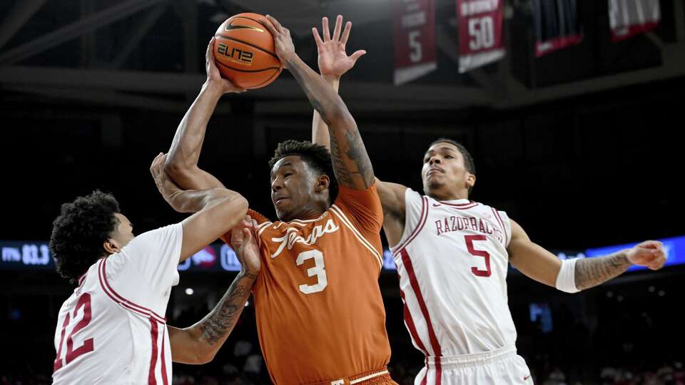 Texas guard Dailyn Swain (3) is fouled as he drives past Arkansas defenders Malique Ewin (12) and Darius Acuff Jr. (5) during the first half of an NCAA college basketball game, Wednesday, March 4, 2026, in Fayetteville, Ark. (AP Photo/Michael Woods)