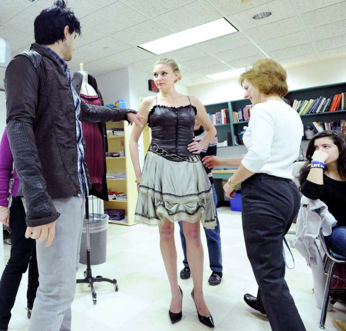 Greenwich fashion designer Jason Troisi, left, who was on the last season of the popular reality show “Project Runway,” shows off one of his dresses on model Anna McGhee as Greenwich High School teacher, Sherry Myer, right, inspects the design during a visit by Troisi to a Greenwich High School fashion design class, Friday morning, Dec. 17, 2010.
