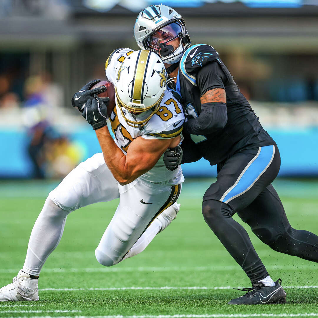 Foster Moreau #87 of the New Orleans Saints takes a hit from Tre'von Moehrig #7 of the Carolina Panthers after a catch during the second half of an NFL game at Bank of America Stadium on November 09, 2025 in Charlotte, North Carolina. 