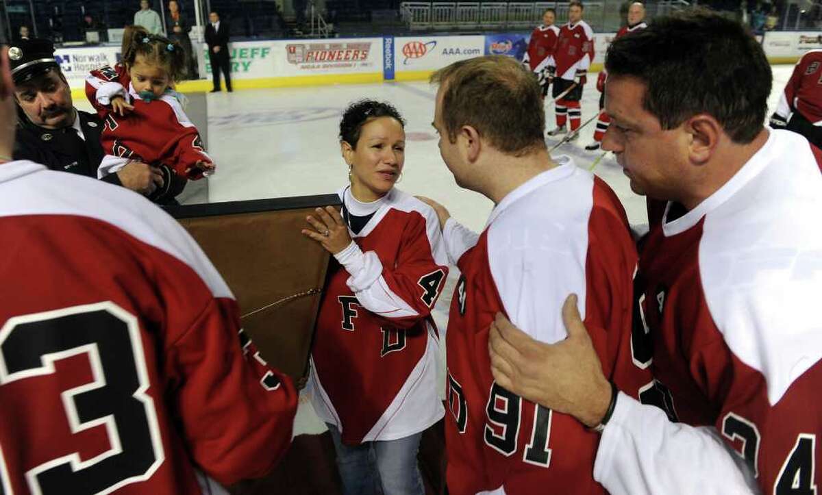 Bridgeport firefighters Jim Buck, center, and Bill Borosky, right, greet Marianne Velasquez in a retirement ceremony for her husband's jersey number, before a charity hockey game between firefighters from the Bridgeport and Worcester, Mass. fire departments was held at the Arena at Harbor Yard in Bridgeport, Conn. on December 18, 2010. The game was held in honor of firefighters Michel Baik and Steven Velasquez, who died fighting a house fire this past July. Velasquez was an active member on the department's hockey team. Proceeds raised from the event go to the Bridgeport Fallen Firefiighters Fund.