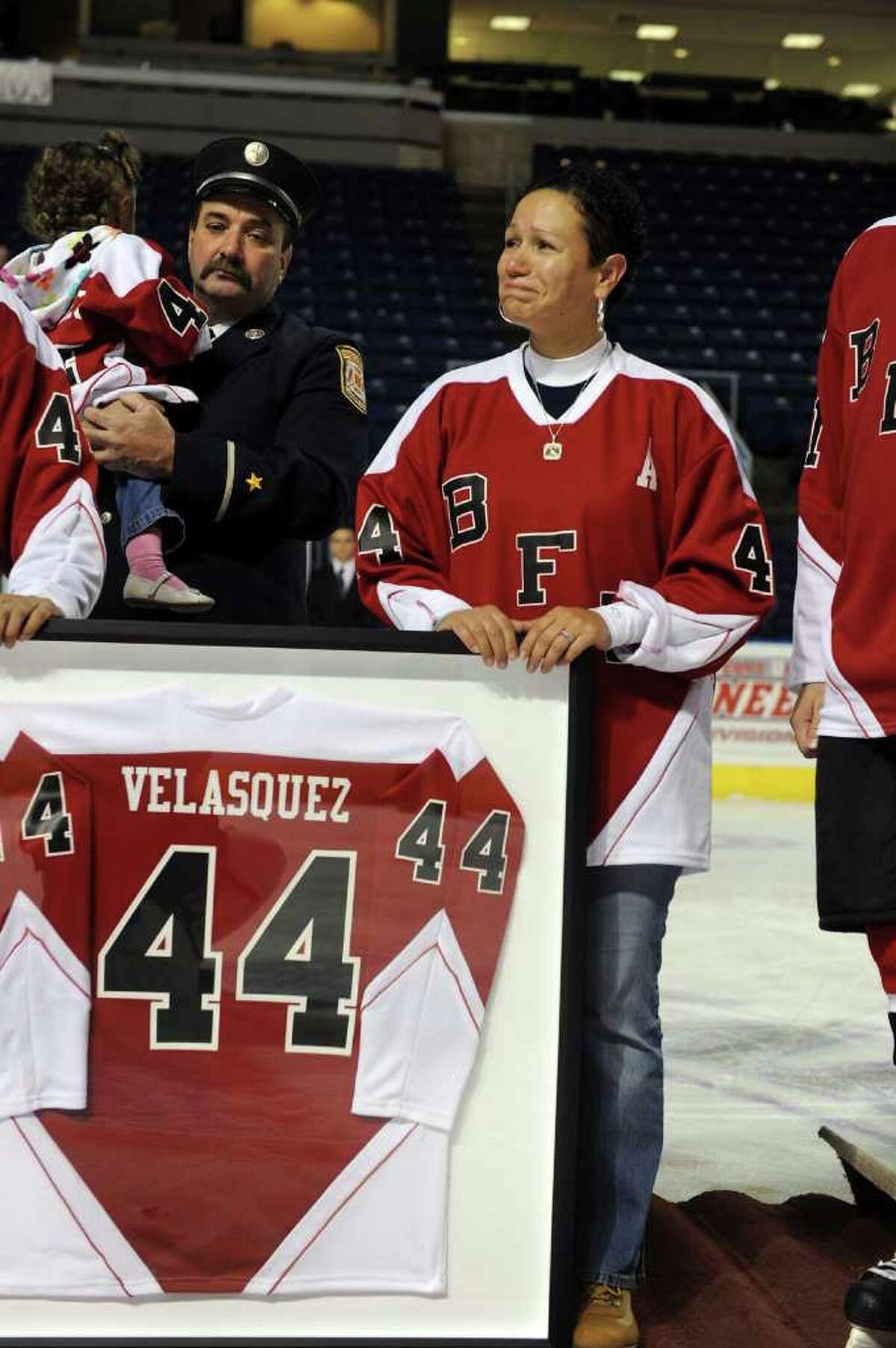 Marianne Velasquez, the widow, of Bridgeport firefighter Lt. Steven Velasquez, holds her husband's jersey which was retired before the start of a charity hockey game between firefighters from the Bridgeport and Worcester, Mass. fire departments was held at the Arena at Harbor Yard in Bridgeport, Conn. on December 18, 2010. The game was held in honor of Velasquez and firefighters Michel Baik, who died fighting a house fire this past July. Velasquez was an active member on the department's hockey team. Proceeds raised from the event go to the Bridgeport Fallen Firefiighters Fund.