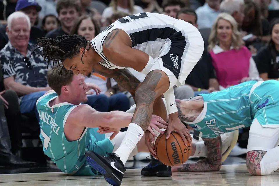 San Antonio Spurs guard Devin Vassell, center, scramble for a loose ball with Charlotte Hornets guard Kon Knueppel (7) and guard LaMelo Ball (1) during the first half of an NBA basketball game in San Antonio, Saturday, March 14, 2026. (AP Photo/Eric Gay)