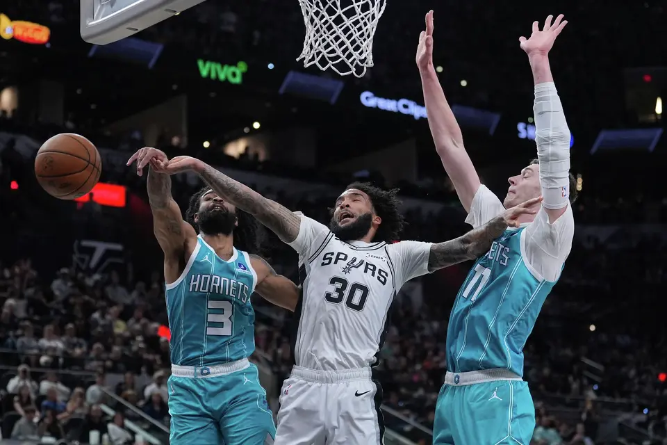 San Antonio Spurs forward Julian Champagnie (30) is blocked by Charlotte Hornets guard Coby White (3) during the first half of an NBA basketball game in San Antonio, Saturday, March 14, 2026. (AP Photo/Eric Gay)