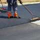 Manual workers helping to level the asphalt surface for a steamroller to press.