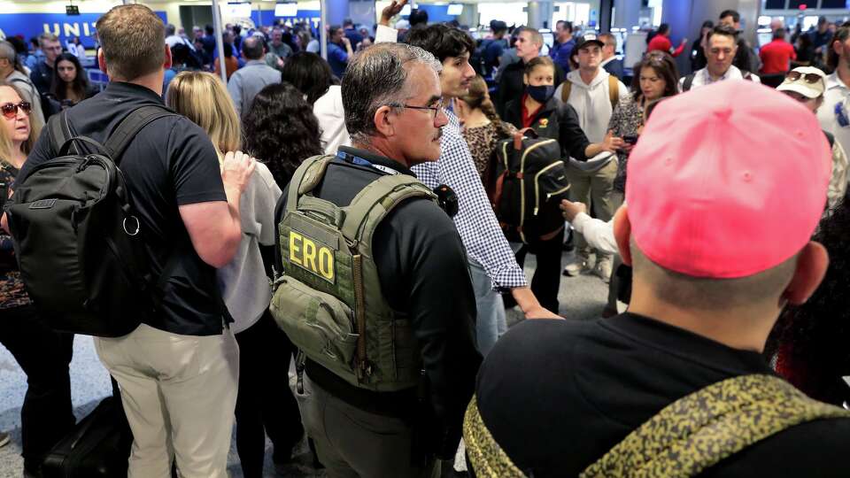 A federal immigration agent stands amid air travelers to assist with security across the lines of people waiting to progress through the TSA checkpoint in Terminal C at the George Bush Intercontinental Airport, Monday, March 23, 2026, in Houston.