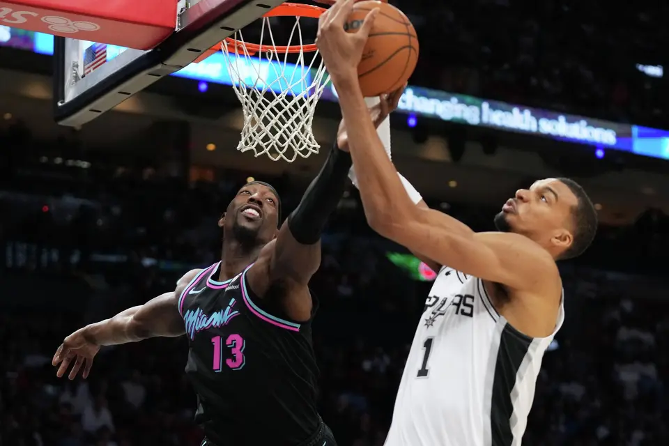 Miami Heat center Bam Adebayo (13) goes for a rebound against San Antonio Spurs forward Victor Wembanyama (1) during the second half of an NBA basketball game, Monday, March 23, 2026, in Miami. (AP Photo/Lynne Sladky)