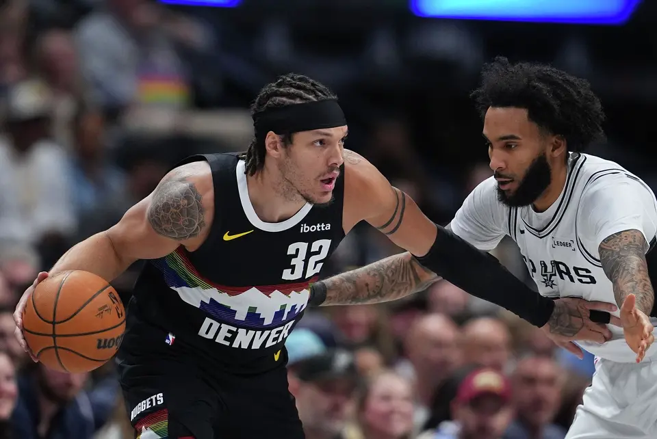 Denver Nuggets forward Aaron Gordon, left, looks to pass the ball as San Antonio Spurs forward Julian Champagnie defends in the first half of an NBA basketball game Saturday, April 4, 2026, in Denver. (AP Photo/David Zalubowski)
