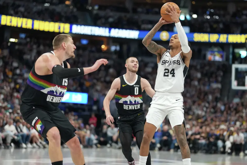 San Antonio Spurs guard Devin Vassell, right, shoots over Denver Nuggets guard Christian Braun (0) and center Nikola Jokic in the first half of an NBA basketball game Saturday, April 4, 2026, in Denver. (AP Photo/David Zalubowski)