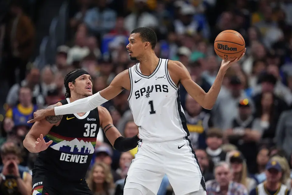 San Antonio Spurs center Victor Wembanyama, right, looks to pass the ball as Denver Nuggets forward Aaron Gordon defends during overtime of an NBA basketball game Saturday, April 4, 2026, in Denver. (AP Photo/David Zalubowski)