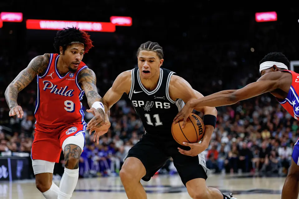 San Antonio Spurs forward Carter Bryant (11) drives past Philadelphia 76ers guard Kelly Oubre Jr. (9) and guard Vj Edgecombe (77) during an NBA game at Frost Bank Center in San Antonio, Monday, April 6, 2026. The San Antonio Spurs defeated the Philadelphia 76ers 115-102.