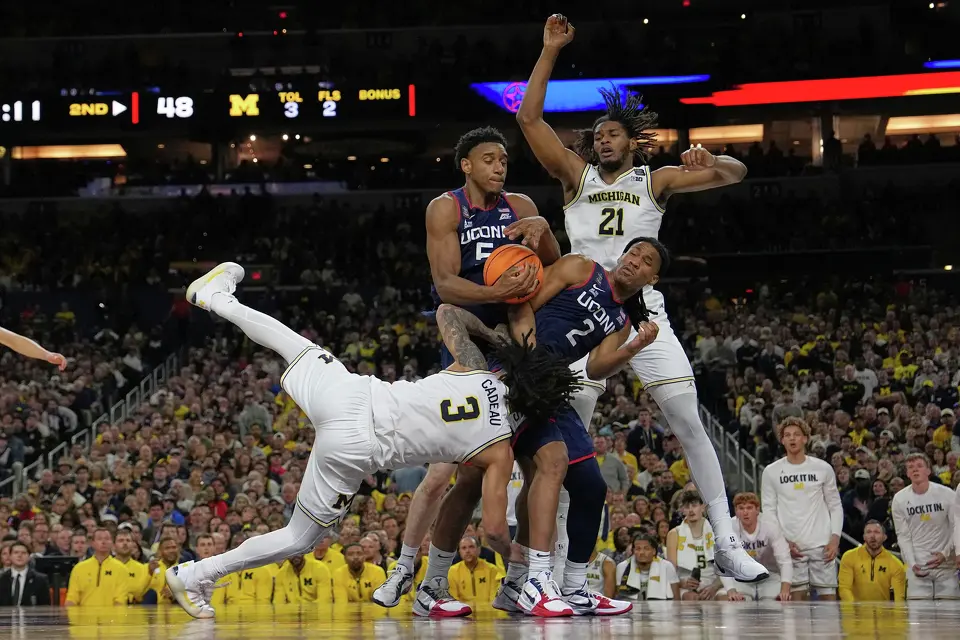 UConn's Tarris Reed Jr. (5) grabs a rebound as Michigan's Elliot Cadeau (3) falls and UConn's Silas Demary Jr. (2) and Michigan's Morez Johnson Jr. (21) watch during the second half of the NCAA college basketball tournament national championship game at the Final Four, Monday, April 6, 2026, in Indianapolis.