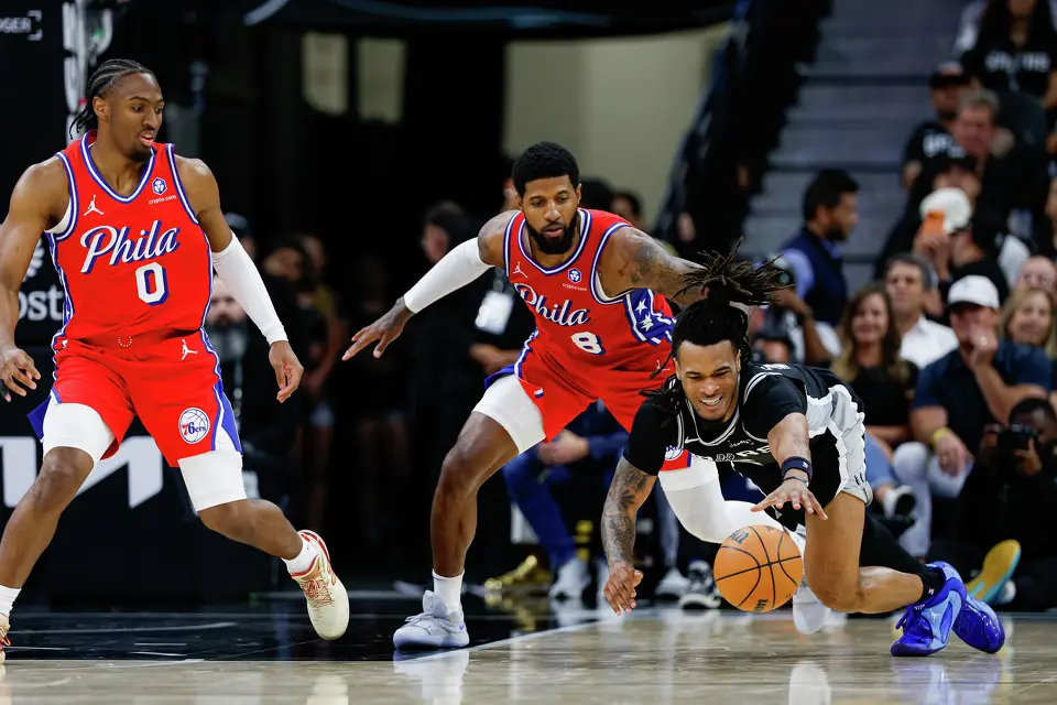 San Antonio Spurs guard Stephon Castle (5) dives for a loose ball in front of Philadelphia 76ers guard Tyrese Maxey (0) and forward Paul George (8) during an NBA game at Frost Bank Center in San Antonio, Monday, April 6, 2026. The Spurs defeated the 76ers 115-102.