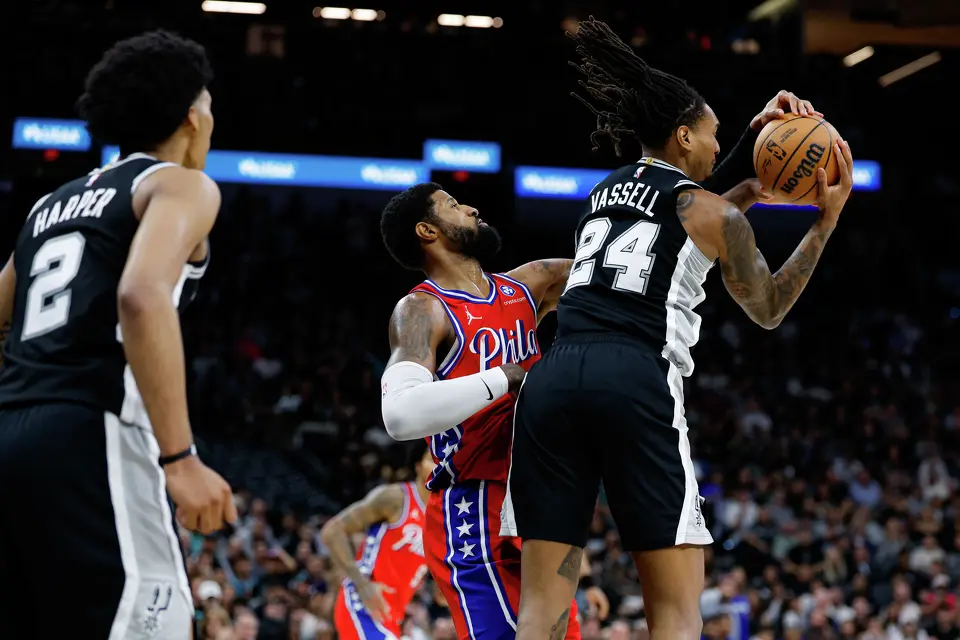 San Antonio Spurs guard Devin Vassell (24) pulls down a rebound over Philadelphia 76ers forward Paul George (8) during an NBA game at Frost Bank Center in San Antonio, Monday, April 6, 2026. The Spurs defeated the 76ers 115-102.