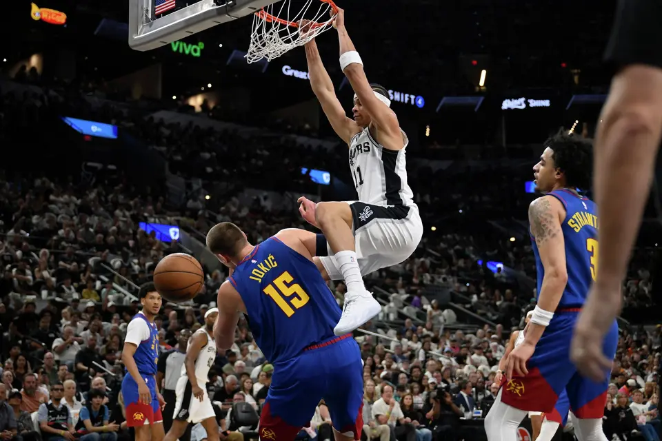 San Antonio Spurs forward Carter Bryant (11) dunks over Denver Nuggets center Nikola Jokic during the first half of an NBA basketball game, Sunday, April 12, 2026, in San Antonio.