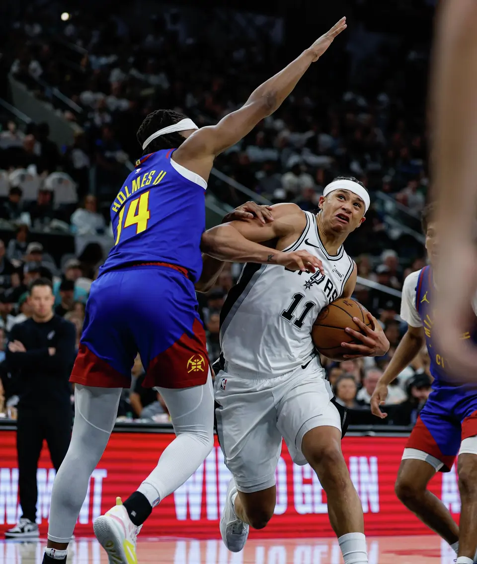 San Antonio Spurs forward Carter Bryant (11) drives to the net around Denver Nuggets forward Daron Holmes II (14) at Frost Bank Center in San Antonio, Sunday, April 12, 2026. The Spurs lost 128-118 to the Nuggets in their final regular-season game.