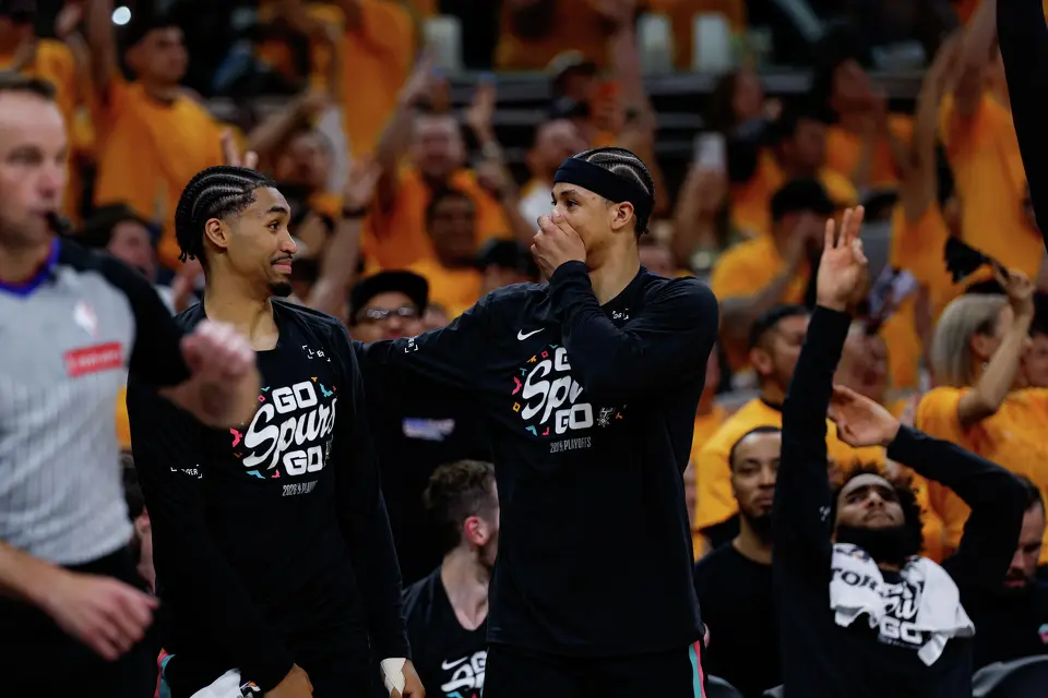 San Antonio Spurs rookies Dylan Harper, left, and Carter Bryant react to a dunk made by San Antonio Spurs forward Victor Wembanyama (1) during the first half of Game 1 of a first-round NBA playoff series at Frost Bank Center, Sunday, April 19, 2026, in San Antonio.