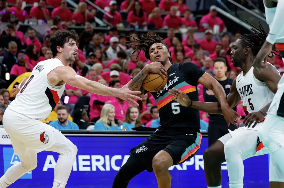 San Antonio Spurs guard Stephon Castle (5) drives past Portland Trail Blazers forward Deni Avdija (8) and guard Jrue Holiday (5) during the first half of Game 1 of a first-round NBA playoff series at Frost Bank Center, Sunday, April 19, 2026, in San Antonio.