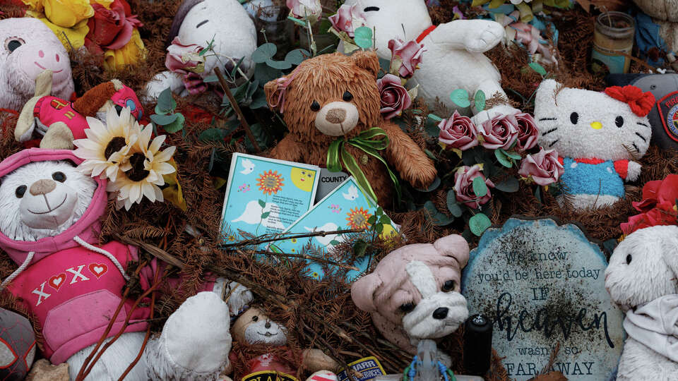 Stuffed animals and other mementos are displayed beneath a wooden memorial cross along Texas 39 near the Guadalupe River and Camp Mystic in Hunt, Texas, on Wednesday, Dec. 3, 2025.