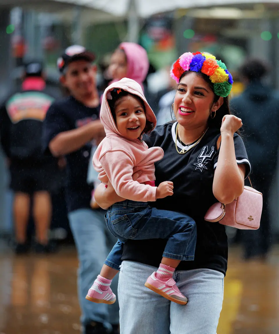 Ashley Rodriguez and her 2-year-old daughter Sloane dodge the rain as they walk into Frost Bank Center for Game 2 of a first-round NBA playoff series between the San Antonio Spurs and the Portland Trail Blazers in San Antonio, Tuesday, April 21, 2026.