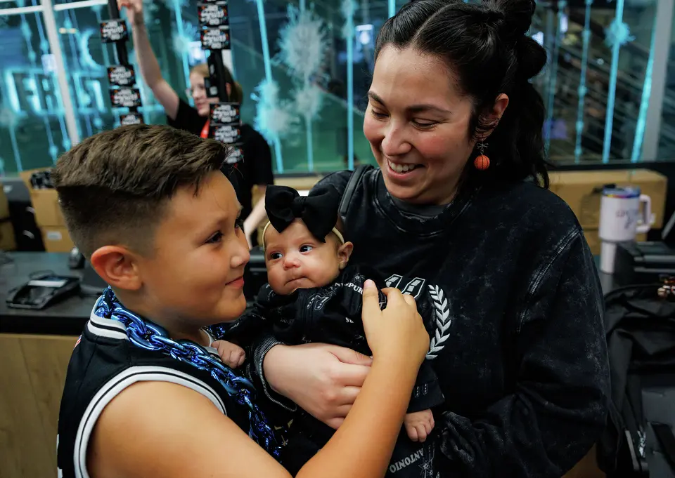 Kassy Gandy holds her 2-month-old daughter, Maizleigh, as her 7-year-old son, Jaxon, hugs his little sister while they wait in line at the fan shop before Game 2 of a first-round NBA playoff series between the San Antonio Spurs and the Portland Trail Blazers at Frost Bank Center in San Antonio, Tuesday, April 21, 2026.