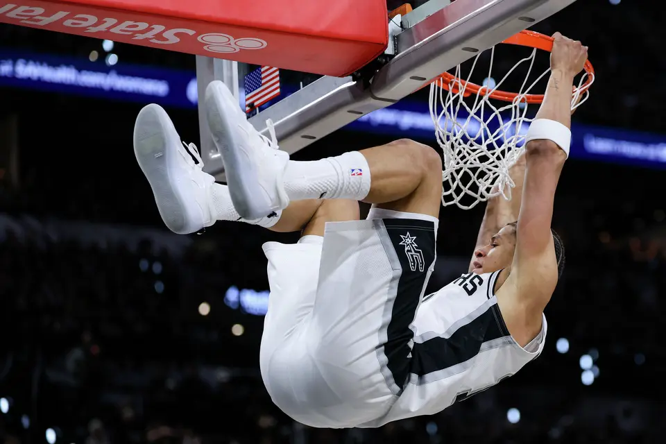 San Antonio Spurs forward Carter Bryant (11) hangs onto the net after dunking on the Portland Trail Blazers during the first half of Game 2 of a first-round NBA playoff series at Frost Bank Center in San Antonio, Tuesday, April 21, 2026.