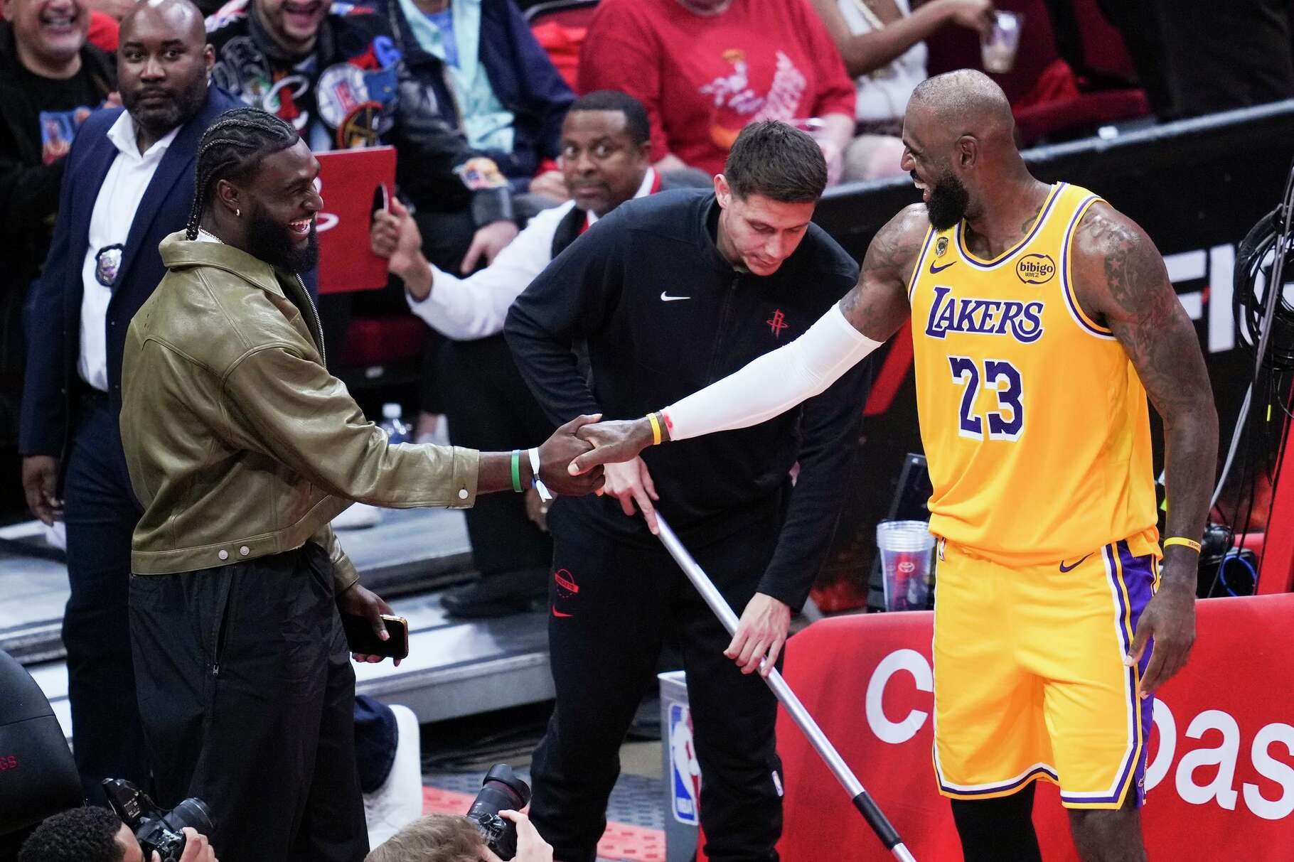 Houston Texans’ Will Anderson, left, laughs with Los Angeles Lakers forward LeBron James after Anderson helped him up out of bounds during the second half in Game 6 of a first-round NBA playoff basketball series at Toyota Center in Houston on Friday, May 1, 2026.