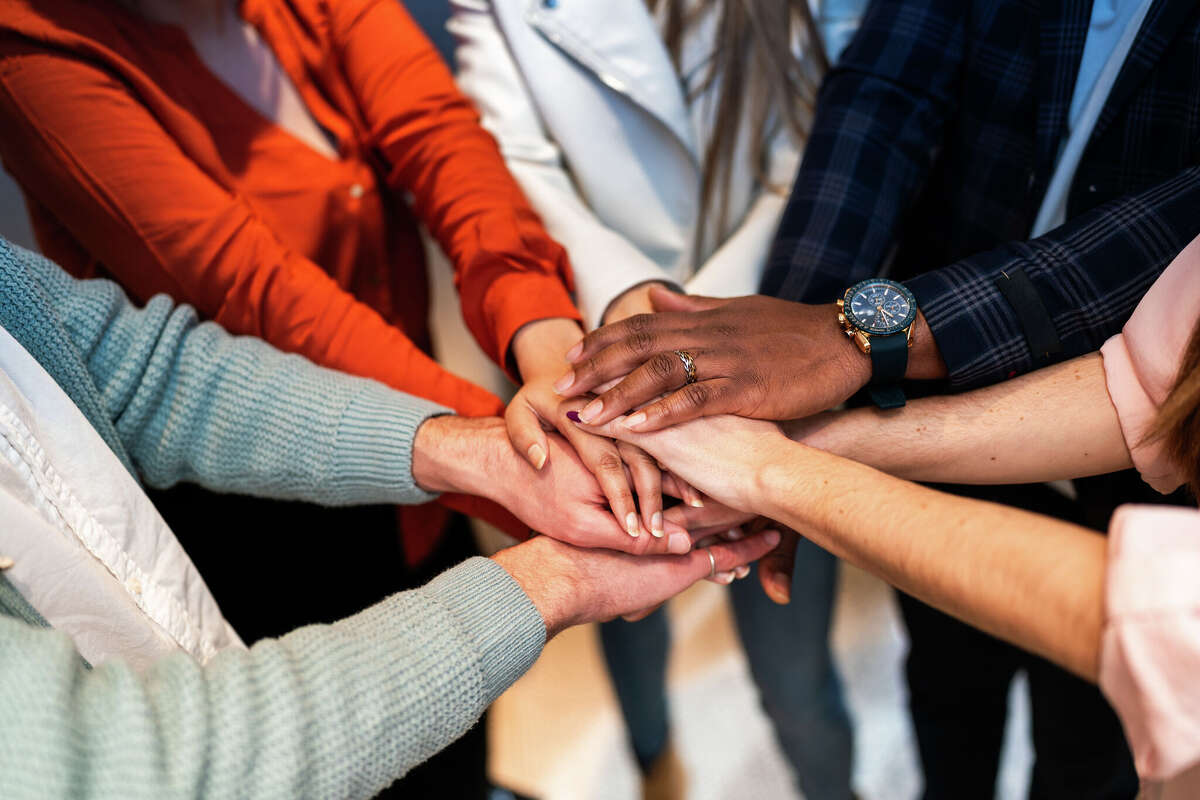 Coworkers joining hands, symbolizing strong teamwork and collaboration while working towards shared goals, embodying unity and support within a diverse corporate environment