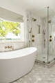 The freestanding tub and glass-enclosed shower are softened by a relaxed Roman shade and warm brass.