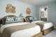 Woven wall art and upholstered beds bring varied texture to this room. Blue walls and pillows continue the home’s nature-inspired palette.