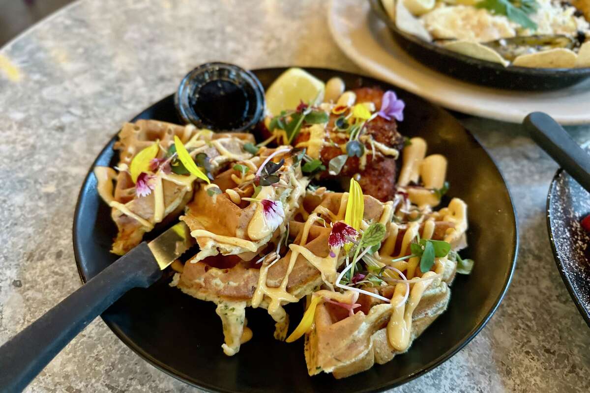 Empire chicken and waffles made with roasted corn, applewood smoked bacon, spinach, and smoked gouda cheese then topped with crispy chicken and sriracha aiolli.