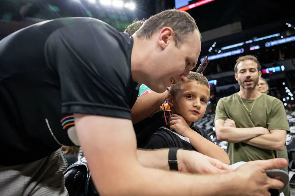 Kyle Willman, left, reacts with his son Ezra Willman, 5, after San Antonio Spurs guard Stephon Castle (5) signed Ezra’s hat prior to the start of Game 4 of the Western Conference Finals at Frost Bank Center in San Antonio on Sunday, May 24, 2026.