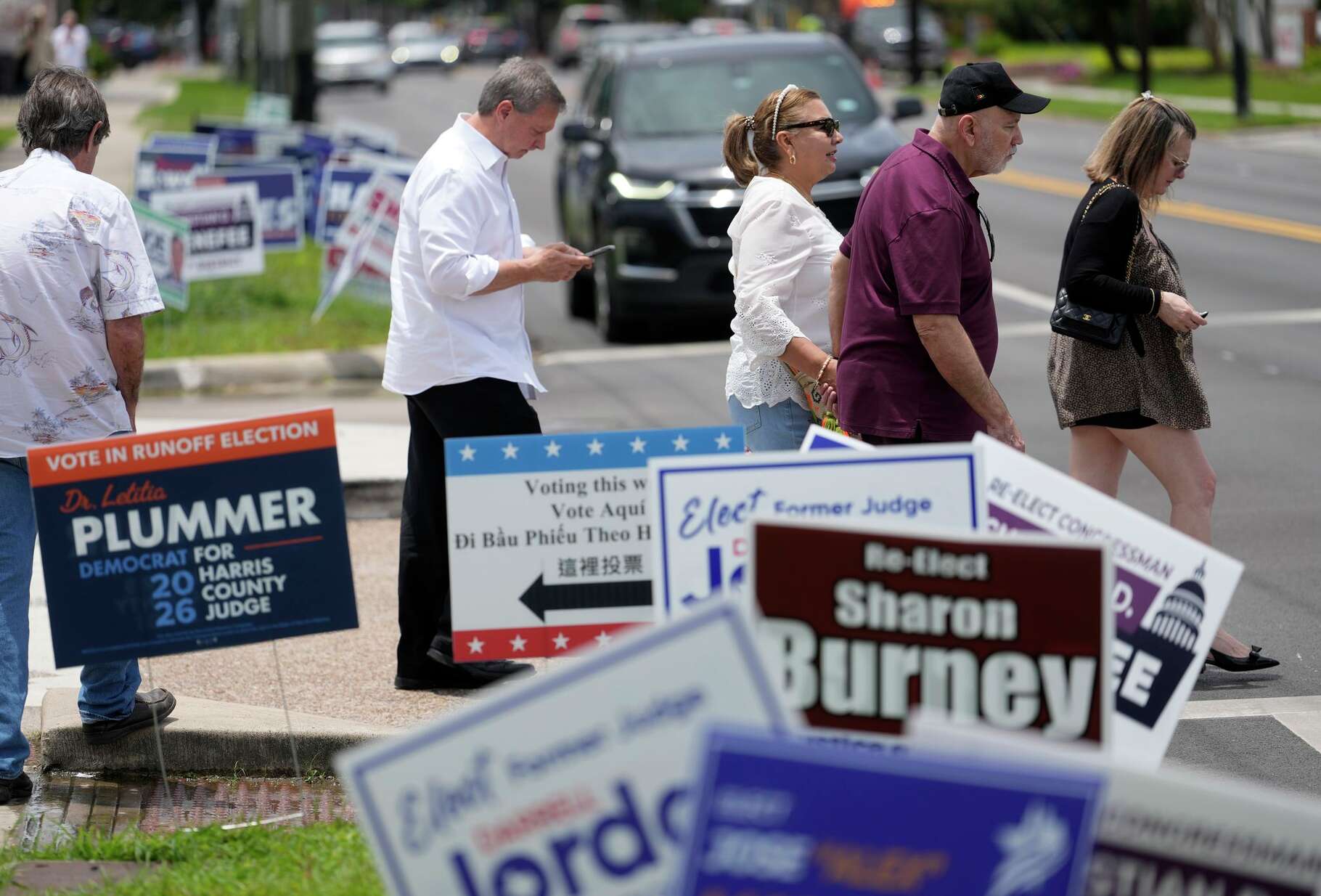People cross the street among campaign signs outside the West Gray Metropolitan Multi-Service Center, a polling site for the Texas primary runoff election, in Houston Tuesday, May 26, 2026.