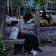 A woman checks her smartphone while sitting on a bench along a sidewalk in northern Tehran, Iran, Tuesday, May 26, 2026.