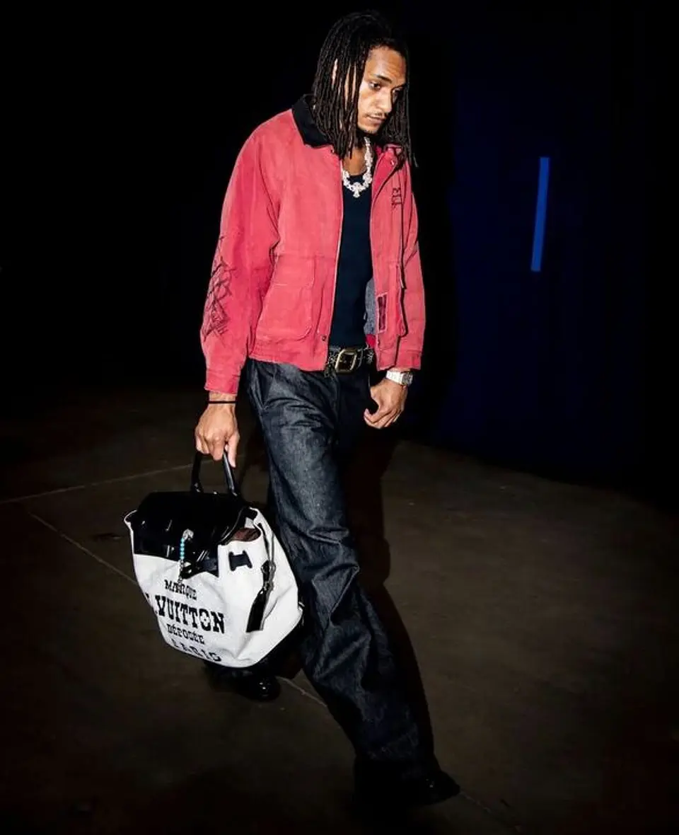 Devin Vassell arrives carrying a Louis Vuitton travel bag while sporting a faded red jacket and dark denim before Game 7.