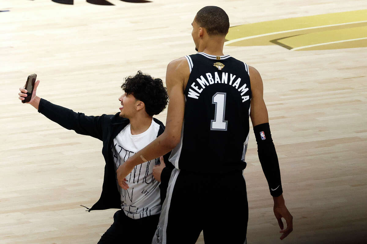 A fan runs onto the court and takes a photo with Victor Wembanyama #1 of the San Antonio Spurs. 