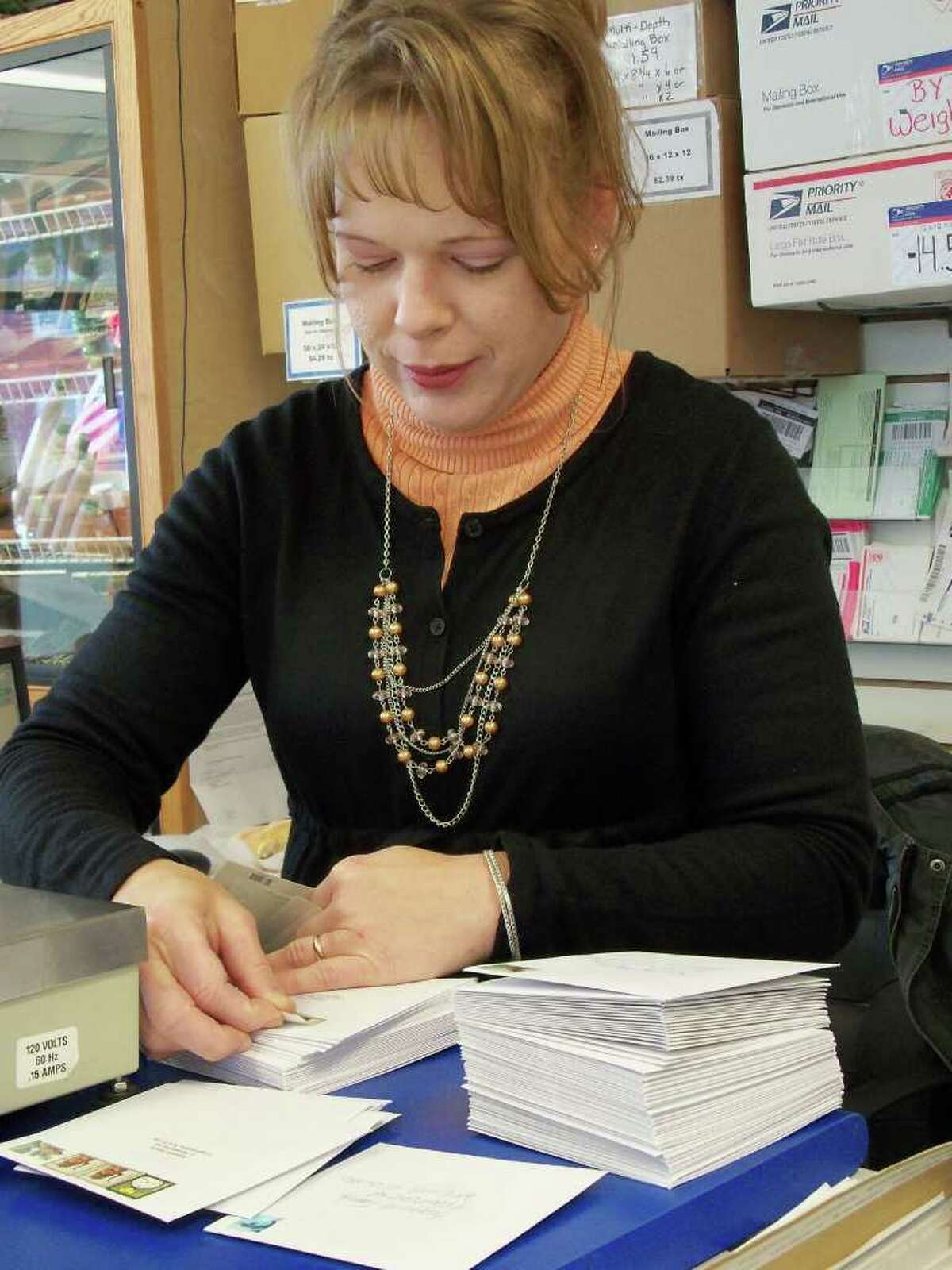 Rebecca Maula, who owns the contract post office in a Riverside Avenue convenience store with her husband, helps out a customer who waited until Tuesday to get Christmas cards in the mail.