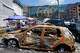 People buy food at an improvised outdoor market, burnt cars in the foreground, surrounded by damaged buildings covered with street artists paintings close to a big city marketplace that was ruined recently by Russian missiles in Kyiv, Ukraine, Monday, June 22, 2026.