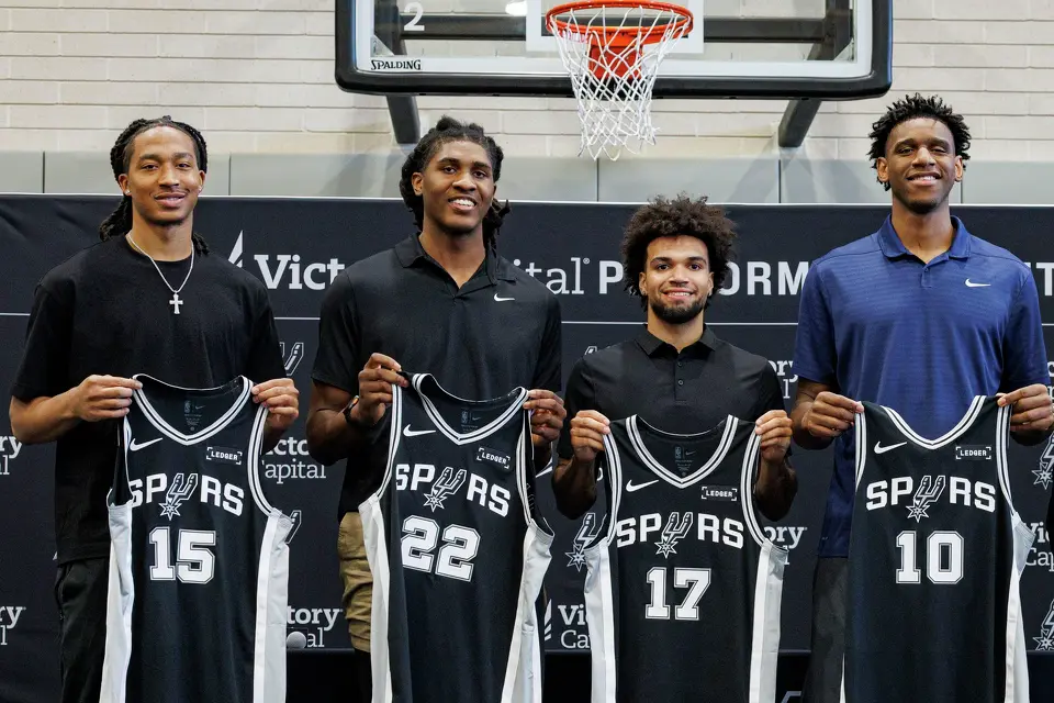 Spurs rookies Maliq Brown, from left, Jayden Quaintance, Ja’Kobi Gillespie and Tarris Reed Jr. hold up their jerseys during an introductory news conference at Victory Capital Performance Center, Thursday, June 25, 2026, in San Antonio.