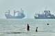 Children wade in the water with cargo ships at anchor in the background and a fisherman nearby, in the Strait of Hormuz off Bandar Abbas, Iran, Tuesday, June 30, 2026. (Amirhosein Khorgooi/ISNA via AP)