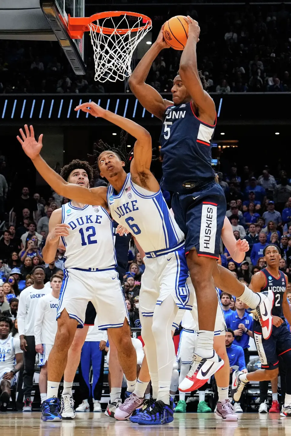 UConn forward Tarris Reed Jr. (5) shoots over Duke forward Maliq Brown (6) as Duke forward Cameron Boozer (12) looks on during the first half in the Elite Eight of the NCAA college basketball tournament, Sunday, March 29, 2026, in Washington. (AP Photo/Abbie Parr)